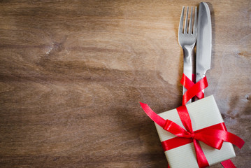 Present and Silverware Decorated with Red Ribbon on Wooden Background.