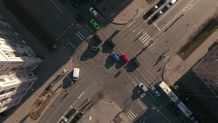 Camera above crossroads in the city, cars drive through the solar part of the road, aerial view. St. Petersburg, Russia