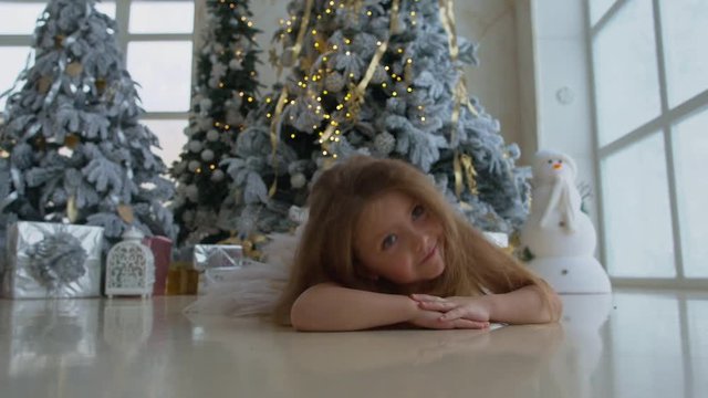 Little happy girl lies near the Christmas tree with gifts