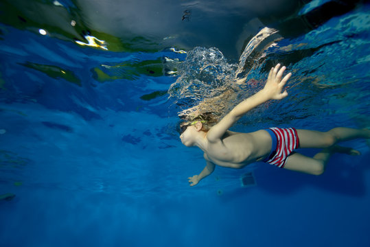 Sports little boy swims underwater in the pool with outstretched arms on a blue background. Portrait. The view from under the water. Landscape orientation