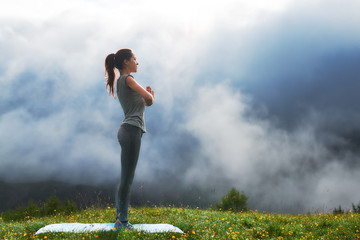 girl doing yoga exercise on lawn in mountains