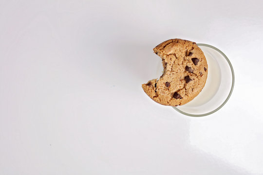 Chocolate Chip Cookie With Bite Eaten And Glass Of Milk On White Background, Minimalism Concept. New Year And Christmas Holiday Background, Copy Space