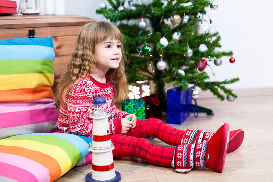 Pretty girl sitting on pillows at Christmas eve, red sweater and fur botos