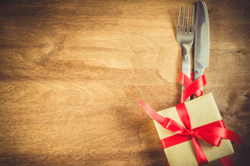 Present and Cutlery Decorated with Red Ribbon on Wooden Background.