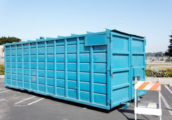 Front and side view of blue industrial dumpster in shopping center parking lot. Horizontal.