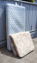 Abandoned mattresses leaning against fence. Vertical.