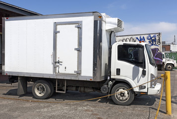Side view of parked white refrigerator truck at loading dock. Horizontal.