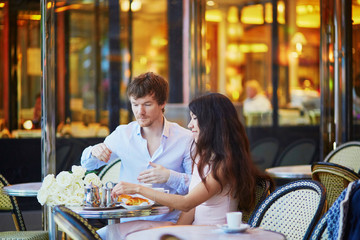 Couple drinking coffee and eating croissants in Parisian cafe