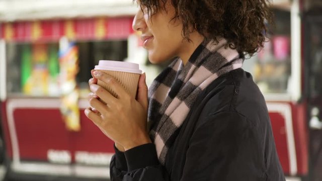 Portrait of young hipster woman holding paper cup, standing by a food stand.