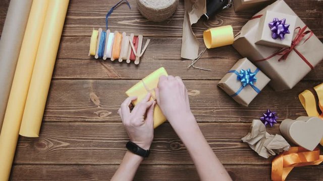 From above shot of crop hands decorating gift box wrapped in yellow paper with simple string.