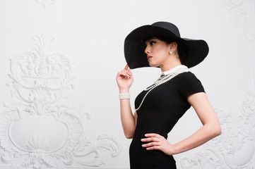 Portrait of a beautiful young woman in retro style in an elegant black hat and dress over luxury...