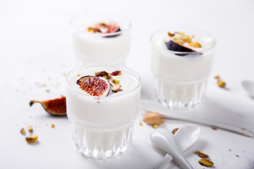 Yogurt in glass cups with nuts,pistachios and fresh figs.Breakfast,Dessert, Pudding on a white background.Food or Healthy diet concept.selective focus.Top view.