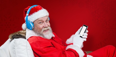 Composite image of santa claus with headphones using phone