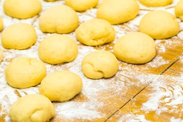 Raw donuts lying in flour on wooden table