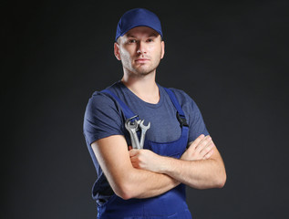 Young mechanic in uniform with crossed arms and wrench standing on a black background