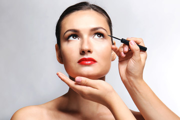 Beautiful girl applying cosmetics on grey background