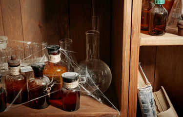 Vintage glass bottles with spiderweb on wooden shelf, closeup