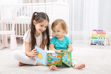 Cute girl reading book with little sister at home