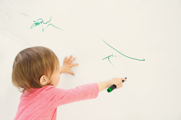 Cute little girl drawing on light wall