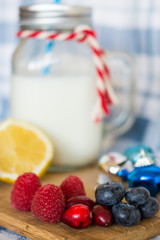 Raspberries, cranberries and blueberries on wooden boards with lemon and milk in the background