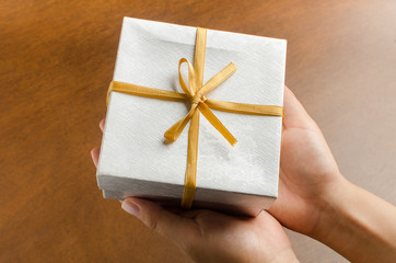Silver gift box with golden ribbon holding by hand to giving in holiday