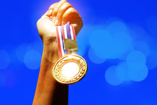 hand raised and holding gold medal against sky, double exposure,