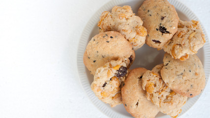 Butter cookies with raisins cornflakes and sesame served on white plate on white background.