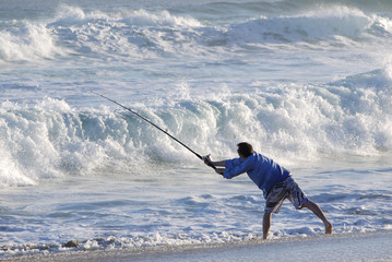 Fisherman casting off into wild surf