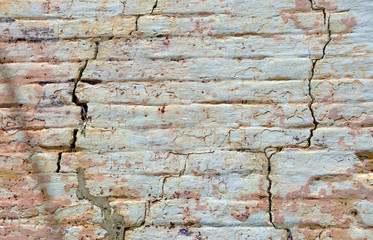 Old cracked rendered wall from historic building with exposed brick and mortar and peeling paint. Grunge texture background with copy space.