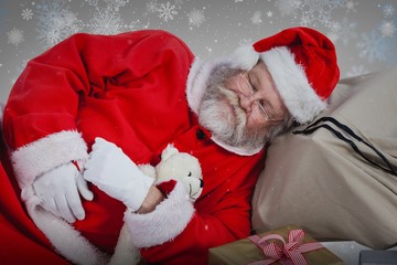 Composite image of tired santa claus sleeping beside christmas p