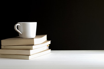 Still life of a cup of coffee put on old books on white wodden table.