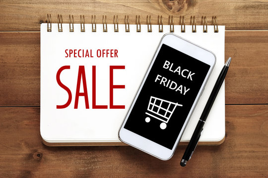 Smart phone with Black Friday Sale on screen over paper notebook