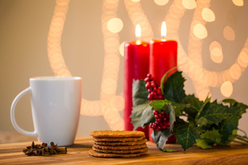 Lovely close up image of Christmas cookies on a wooden chopping board with some scented candles and a glass of whiskey / coffee and some cinnamon sticks.