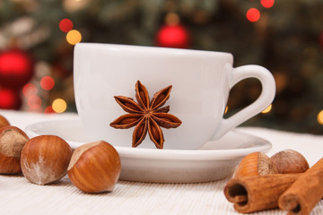 Hazelnuts, spices, cup of coffee or tea and christmas tree with lights in background