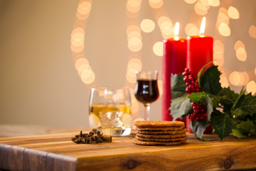 Lovely close up image of Christmas cookies on a wooden chopping board with some scented candles and a glass of whiskey / coffee and some cinnamon sticks.