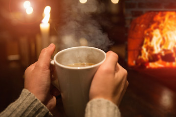 woman's hands with a cup of coffee. The evening, candles are lit, dark, romantic.