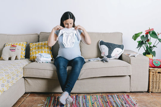 Pregnant woman sitting on couch, looking at baby sleepers