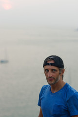 Happy Young Bearded Man standing on view point with a seascape wearing in blank blue t-shirt and black Cap