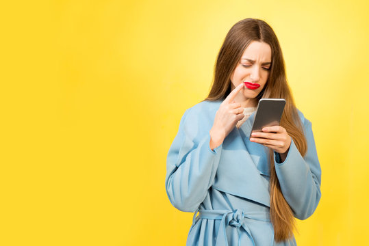 Portrait Of Confused Woman With Mobile Phone On The Yellow Background