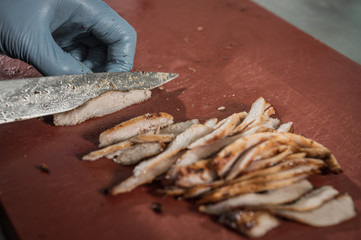 .Male chef is standing sliced meat with a sharp knife on a wooden board in the kitchen