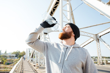 Portrait of a young bearded athlete in sportswear drinking water