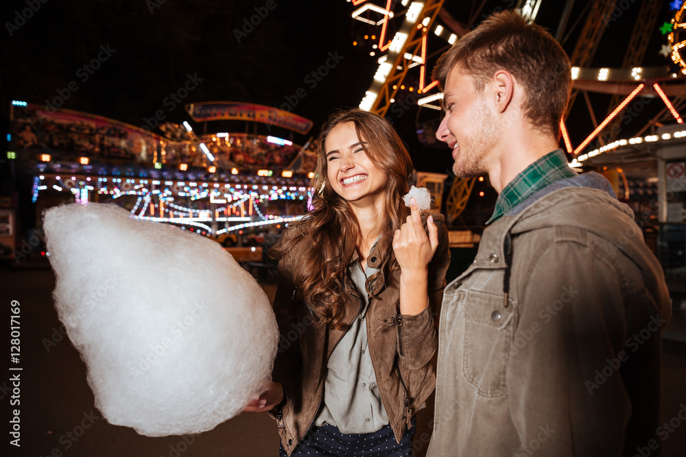 Wall mural Couple eating cotton candy and laughing in amusement park