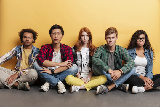 Multiethnic group of serious young people sitting with legs crossed