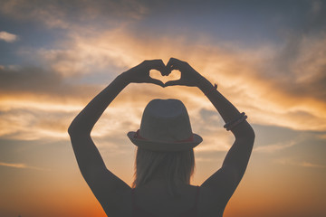 Silhouette of a girl making a heart-shape.