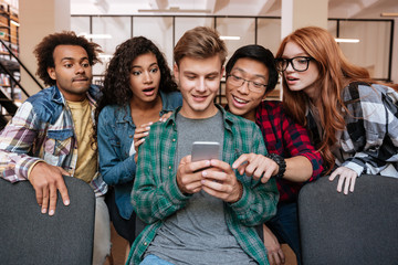 Cheerful young man using smartphone with his amazed friends