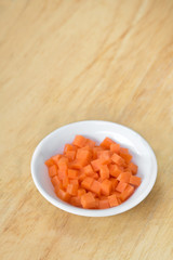 Carrot cubes in white cup on wooden cutting board