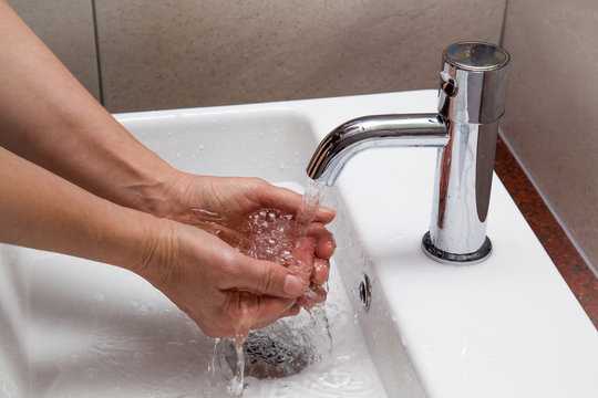 Hygiene. Woman washing her hands in the ceramic sink under the water tap. Water running. Healthy lifestyle.
