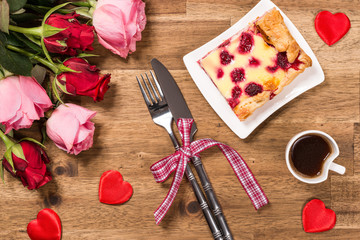 Raspberry cake on white plate, coffee, roses and red hearts on wooden background. Valentines Day background