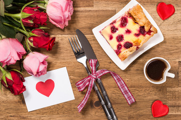 Raspberry cake on white plate, coffee, roses and red hearts on wooden background. Valentines Day background