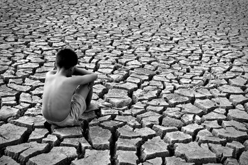 Sad a boy sitting on dry ground .concept drought and hope - obrazy, fototapety, plakaty